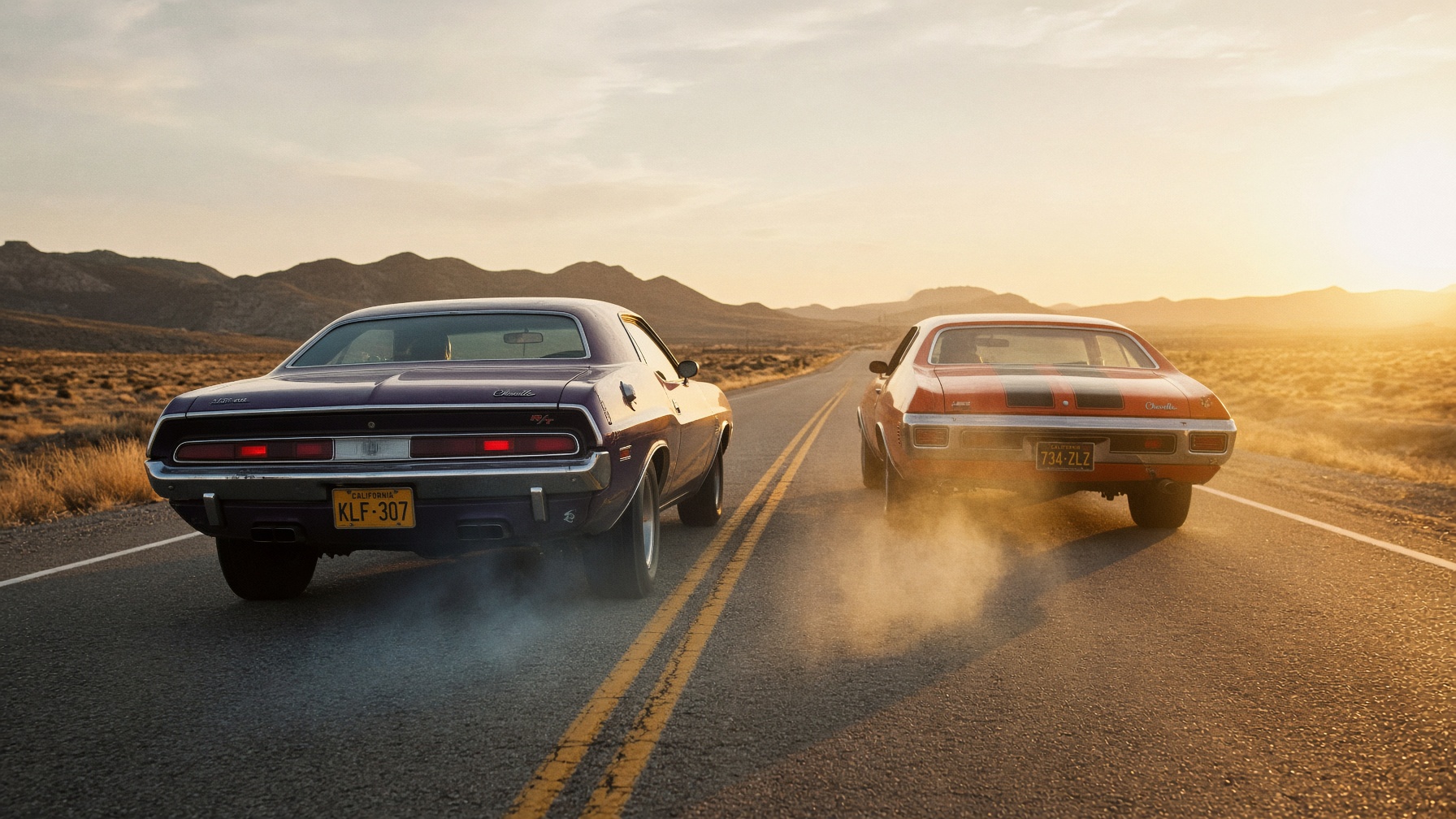 Two 1970s muscle cars on a desert highway at sunset